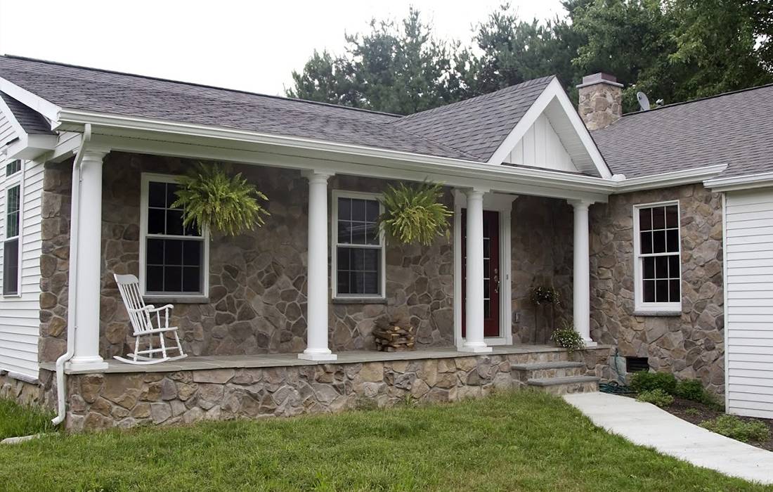 the front of a new stone house, with a covered patio & shingled roof