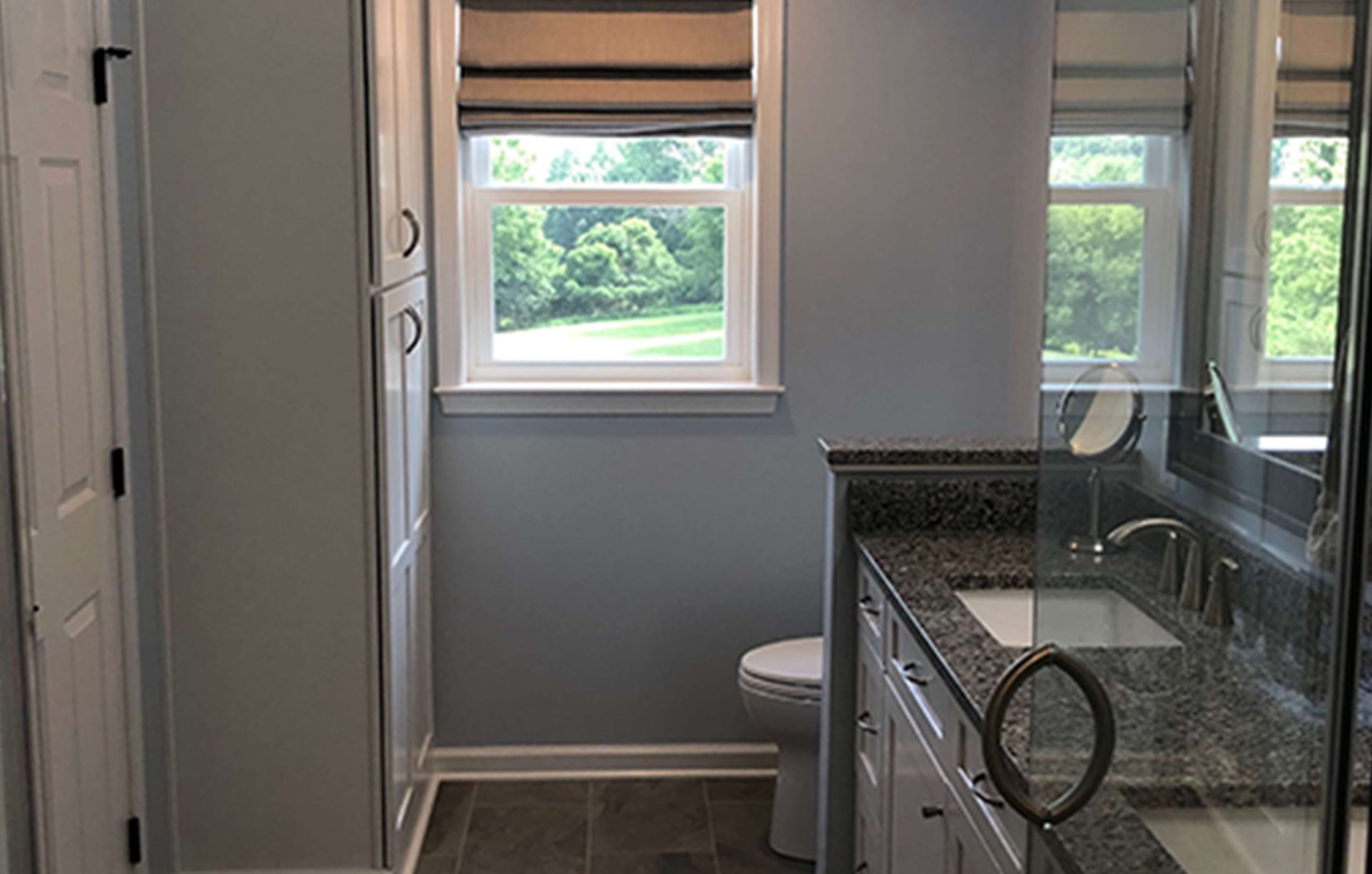 a remodelled bathroom with a granite vanity sink, tile floors, & a glass-walled shower