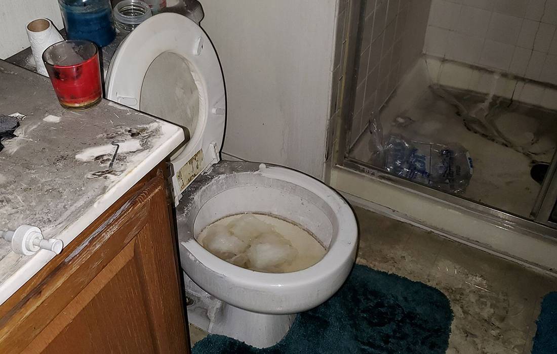 a fire-damaged bathroom with a burnt counter, toilet, & shower before restoration